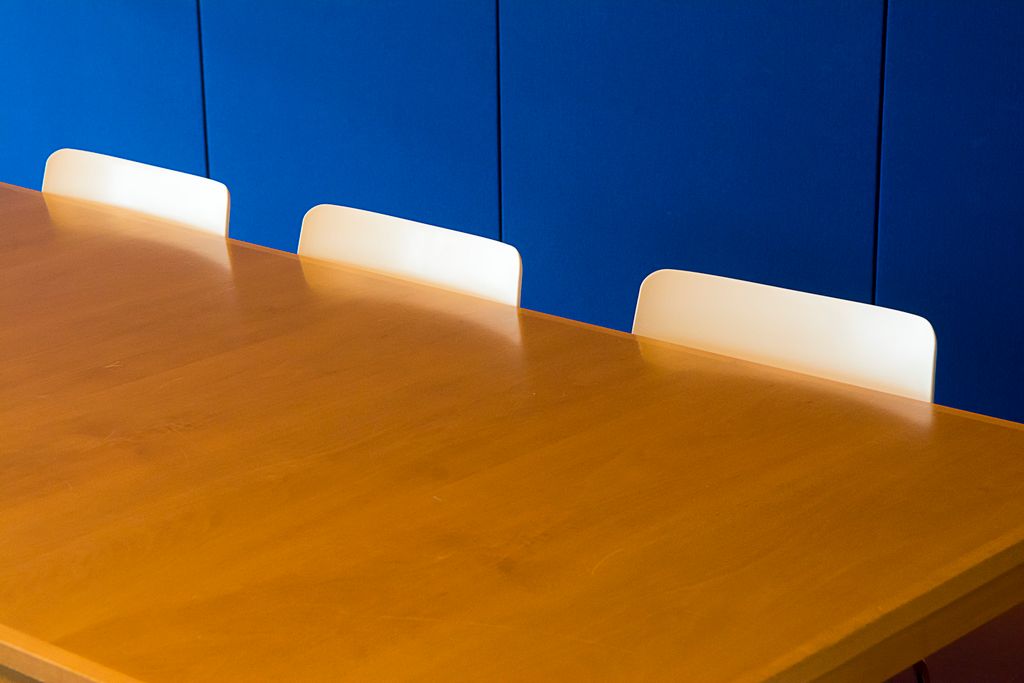 Empty wooden meeting table with white chairs against a deep blue wall