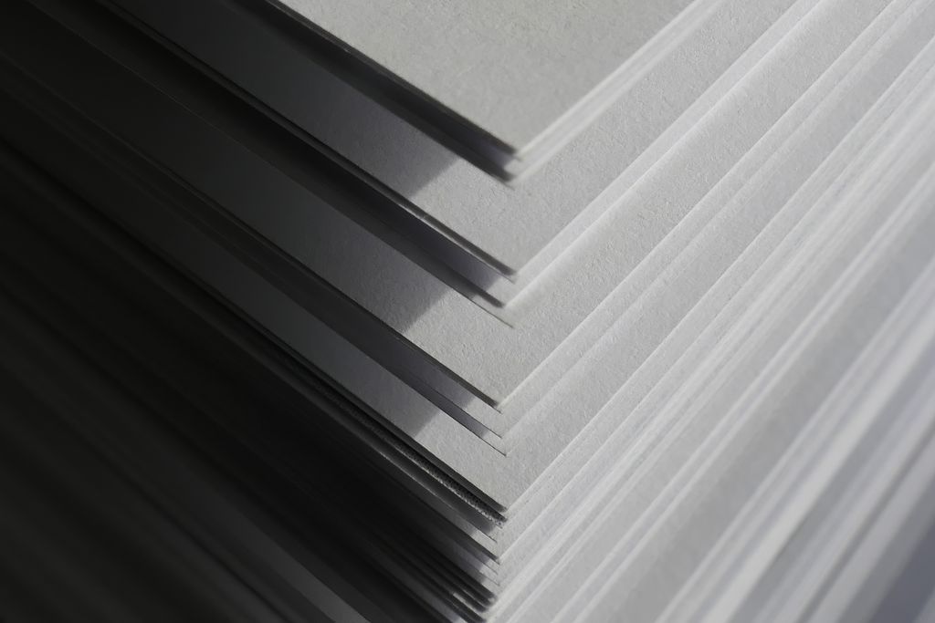 Close-up of the corner of a neat stack of paper sheets in soft gray light, representing a procurement package
