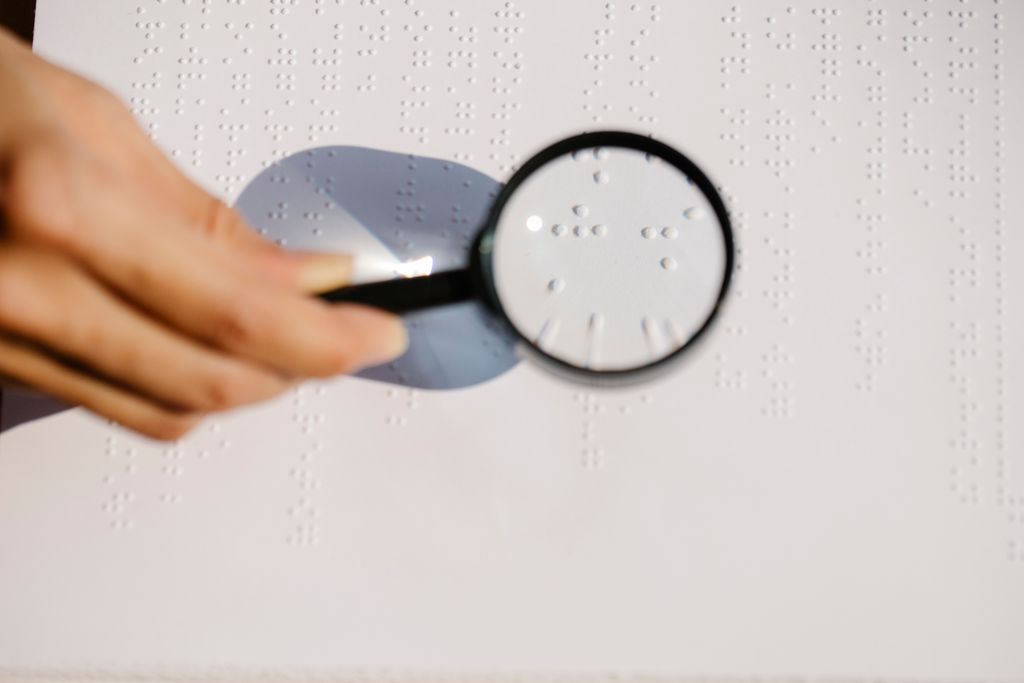 Hand holding a magnifying glass over a white sheet of raised braille dots, suggesting inspection rather than repair