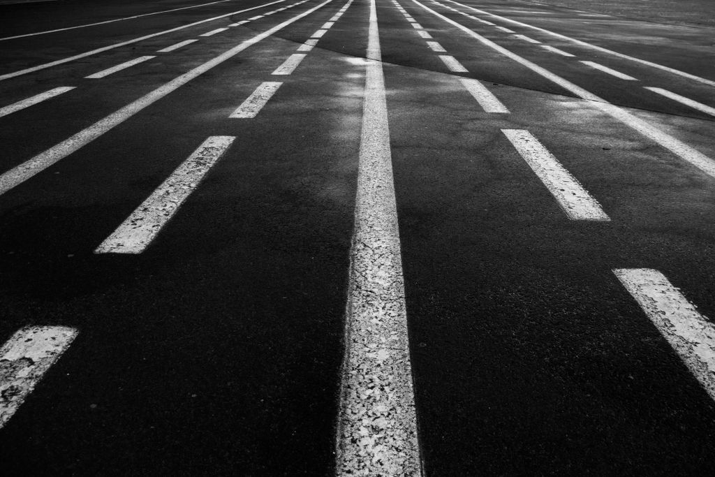 Grayscale asphalt road with white lane lines stretching toward the horizon, representing a staged path forward