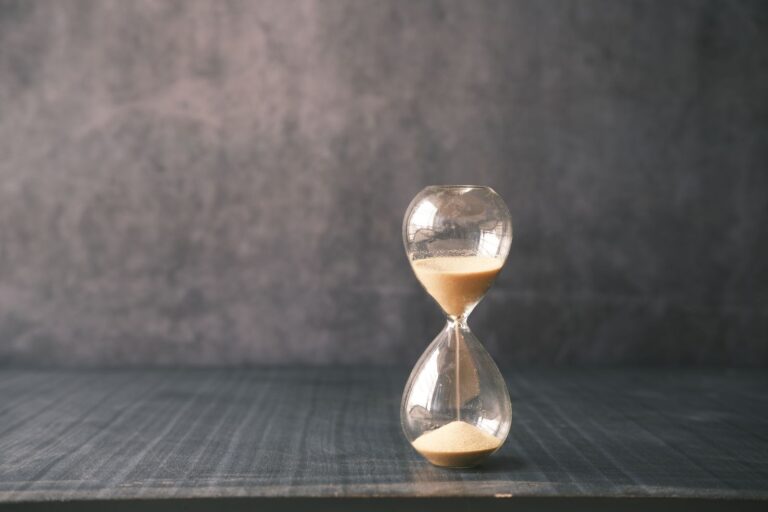 Glass hourglass with pale sand running through it on a dark wooden table