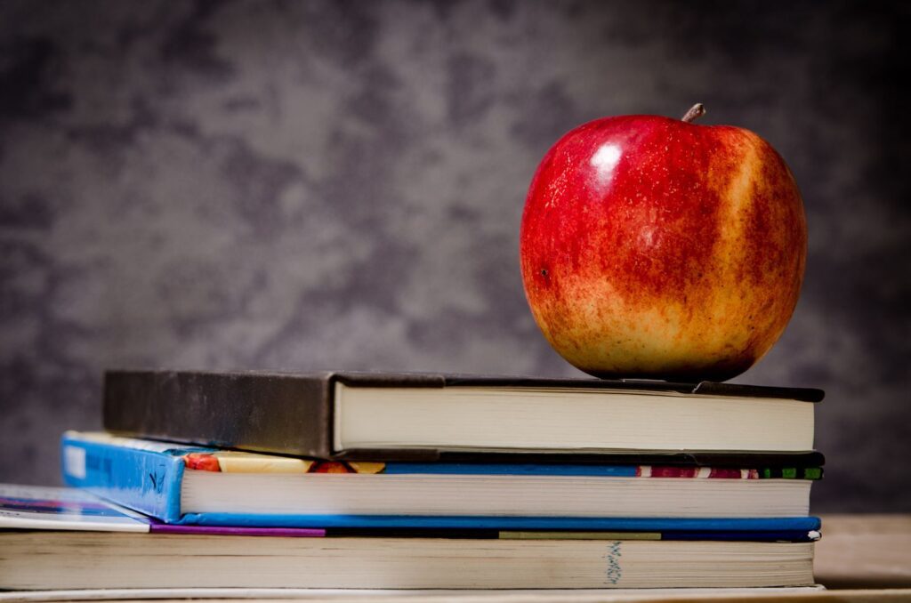 Red apple resting on a stack of hardcover books against a gray backdrop