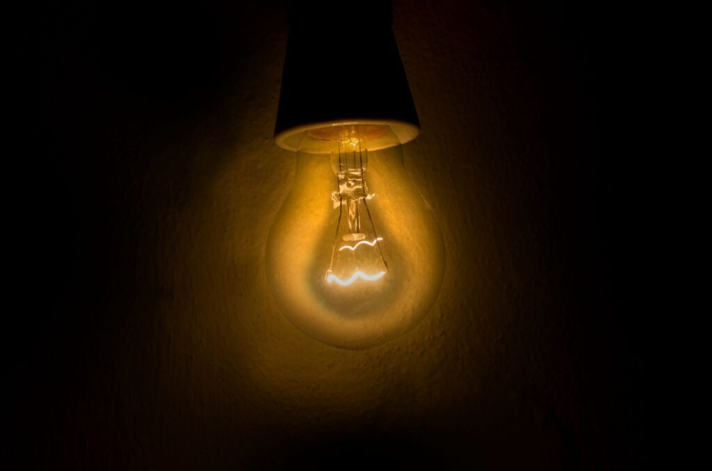 Bare incandescent light bulb glowing warm orange in a dark room