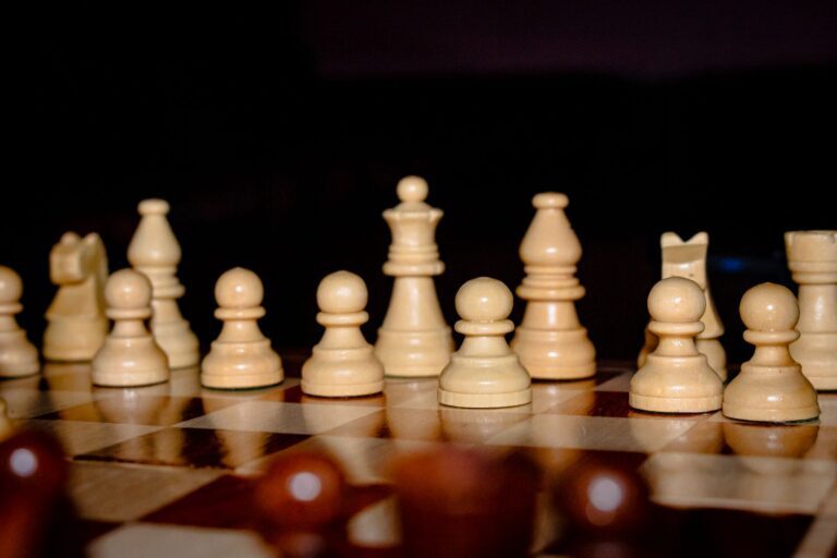 Cream chess pieces lined up on a polished board against a dark background