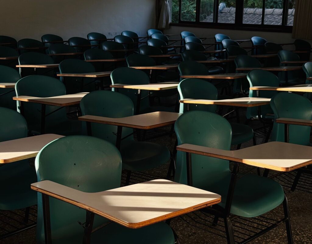 Empty classroom filled with rows of green chairs with attached wooden desks