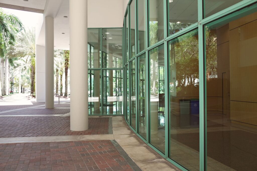 Modern campus building with green-framed glass walls and white columns along a brick walkway