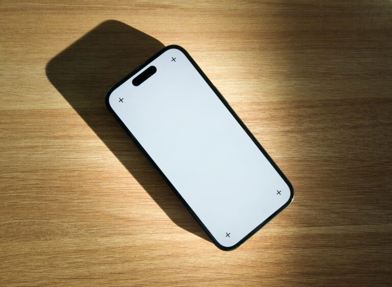 Smartphone with a blank white screen lying on a sunlit wooden table