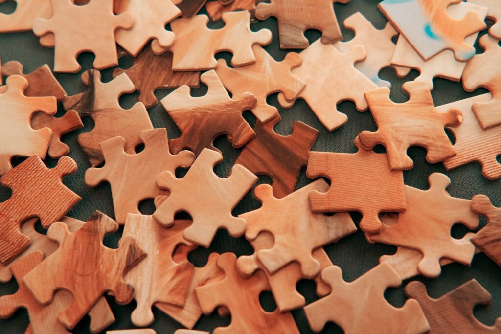 Scattered wooden jigsaw puzzle pieces in light and dark tones on a dark surface