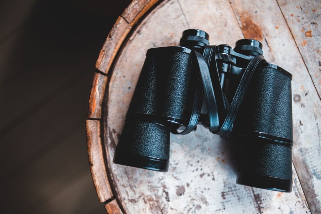 Black binoculars resting on a weathered round wooden tabletop