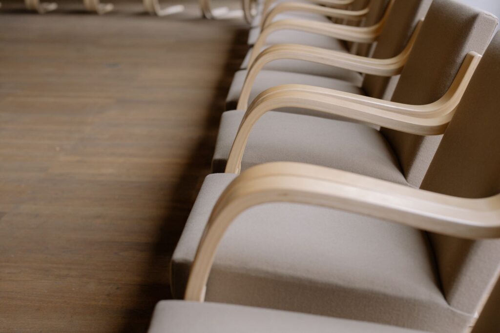 Row of empty upholstered chairs with curved wooden arms on a wooden floor