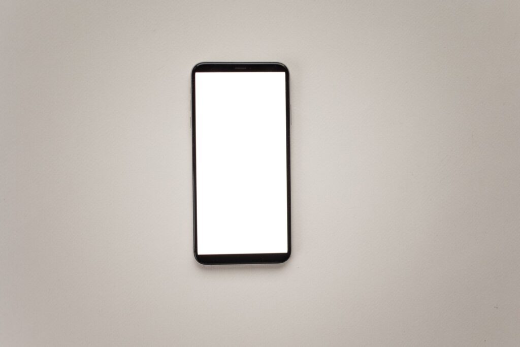 Black smartphone with a blank white screen centered on a light gray surface