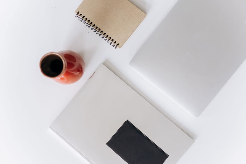 Top-down view of a white desk with notebooks, a closed laptop and a red cup