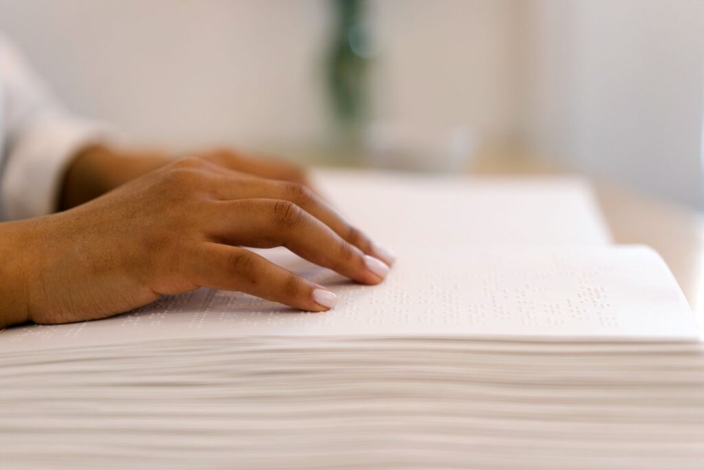 Hand gliding fingertips across the raised dots of an open braille book
